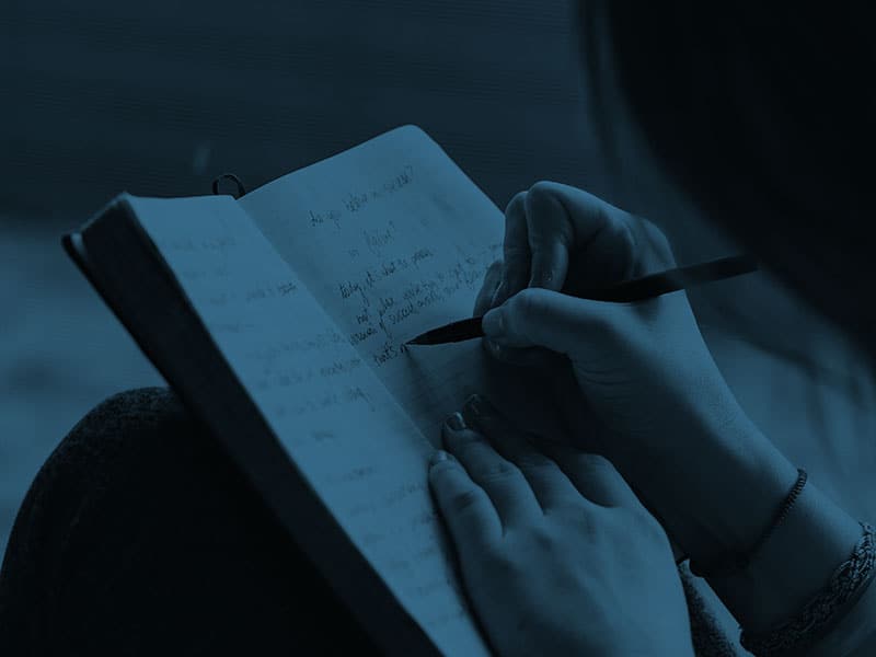 A person writing in a notebook with a pen.